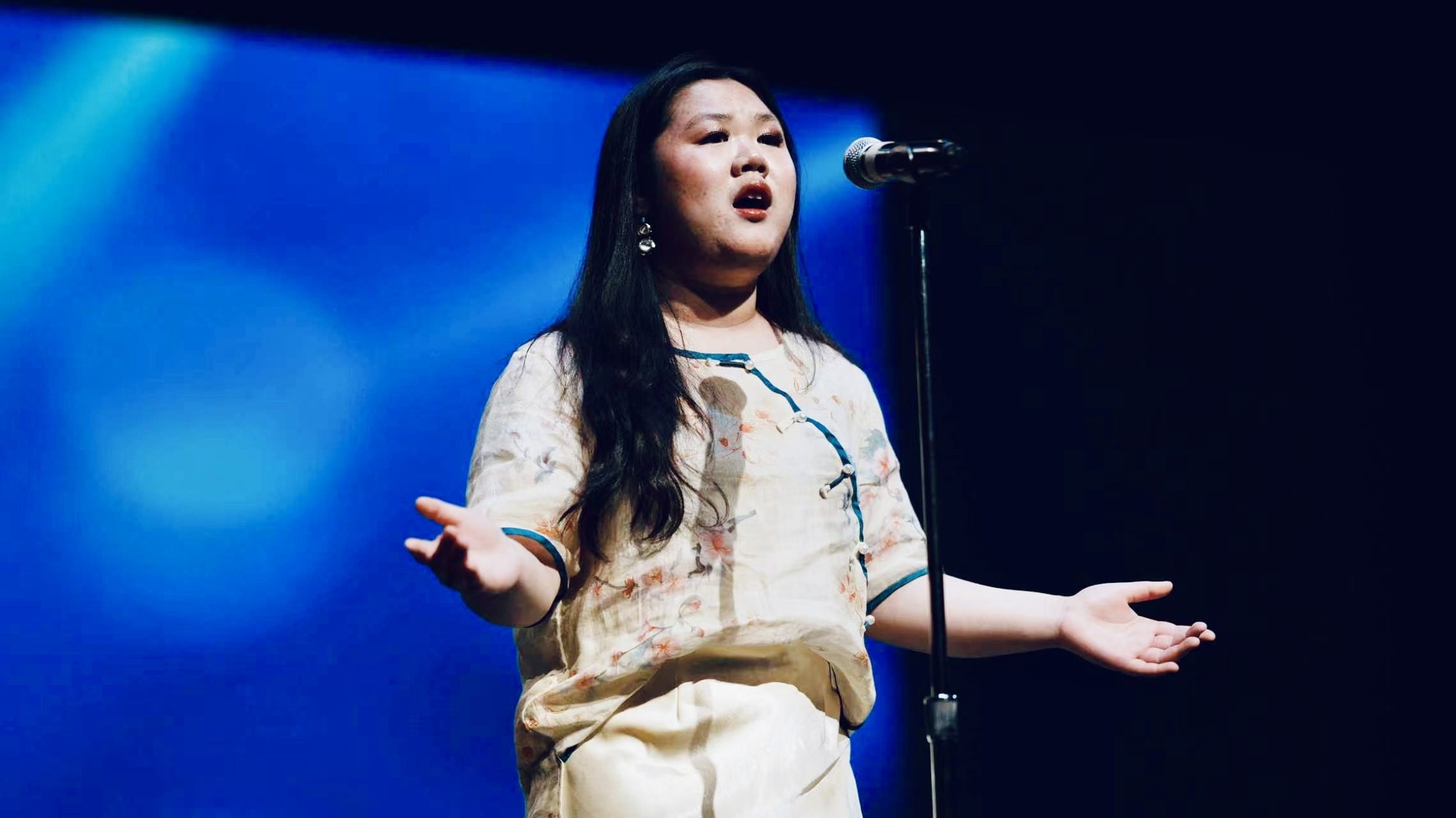 Lesslie Li singing at a microphone on a blue-lit stage